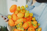 一名女子拿着一束充满活力的橙色毛茛花束，正在使用智能手机