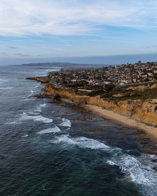 A stunning aerial shot of a coastal town with rugged cliffs and waves crashing on the shore.