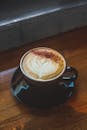 一杯温暖的拿铁咖啡，带着复杂的艺术感，装在木桌上的黑色杯子里