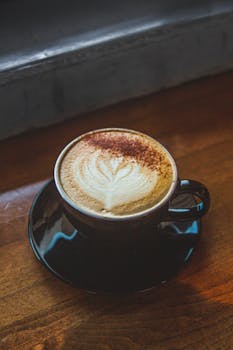 一杯温暖的拿铁咖啡，带着复杂的艺术感，装在木桌上的黑色杯子里