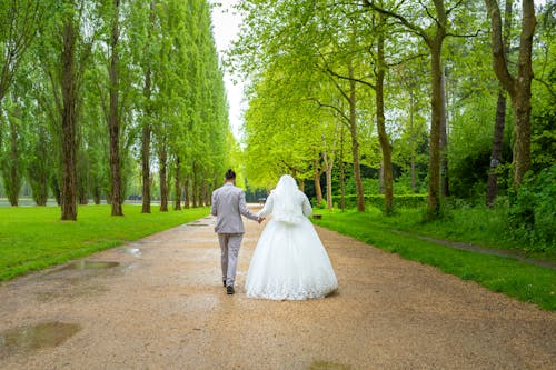 A bride and groom walking down a path in the park