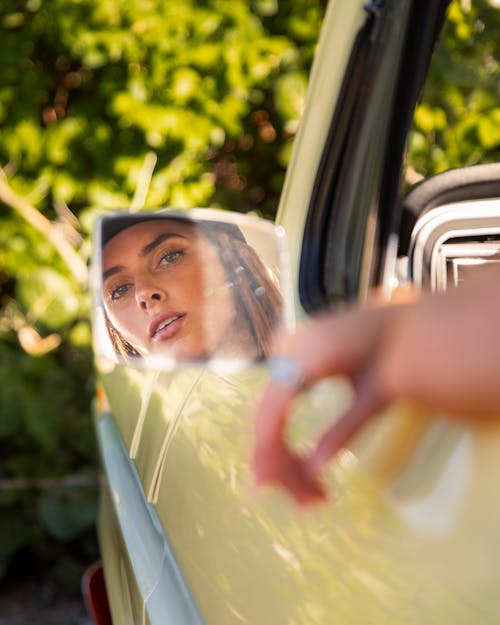 A woman looking in the mirror of a yellow car