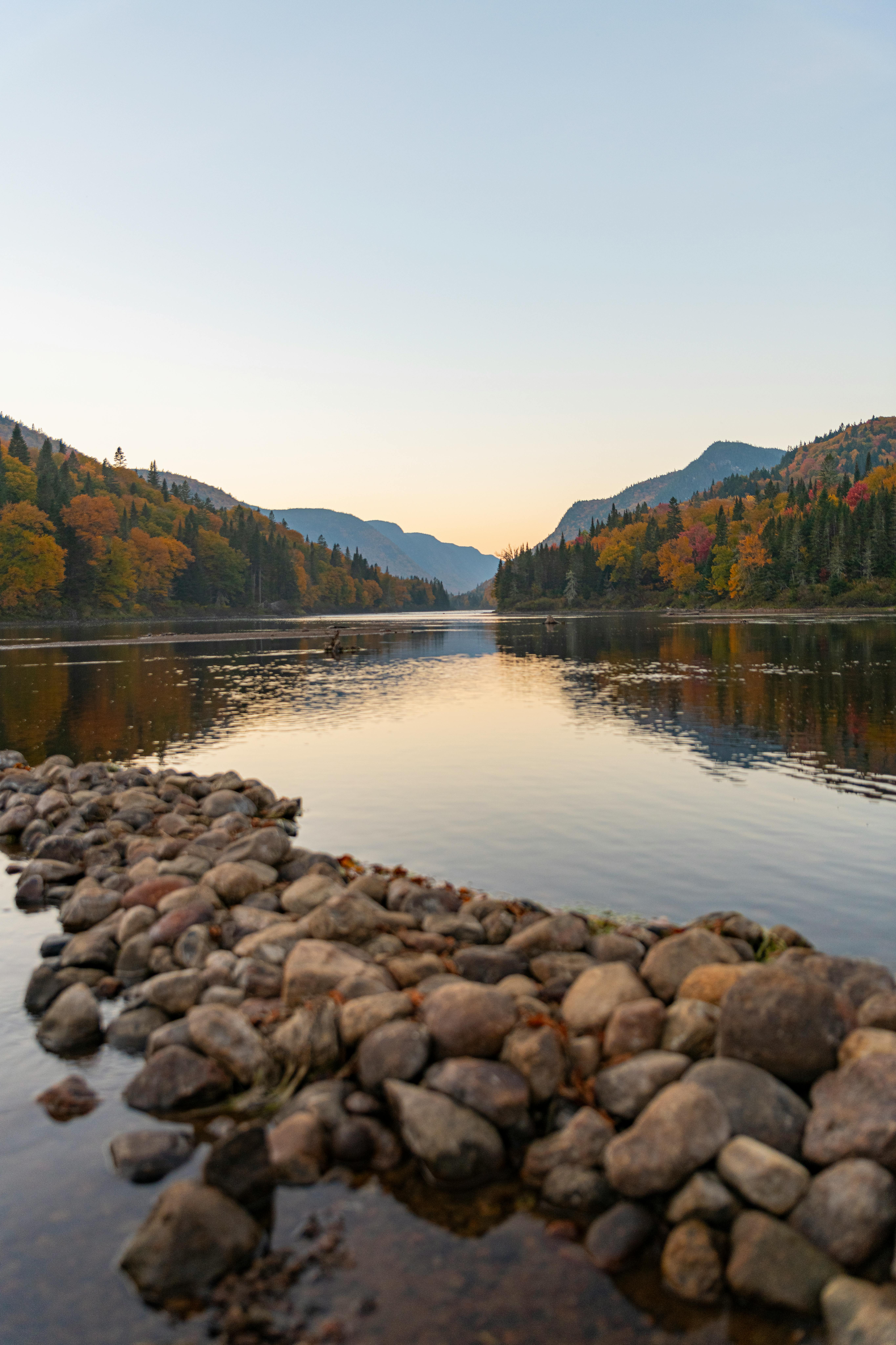 Tranquil autumn lake surrounded by colorful trees and rocks, reflecting a calm sky.