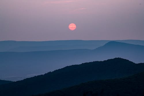 A sunset over a mountain range with a bright red sun