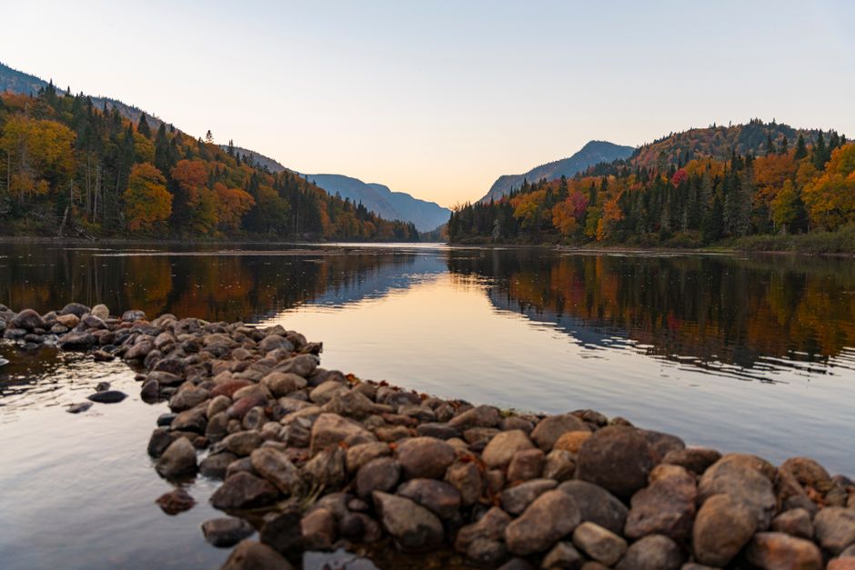 Peaceful autumn scene with colorful trees reflected in a lake at sunset.
