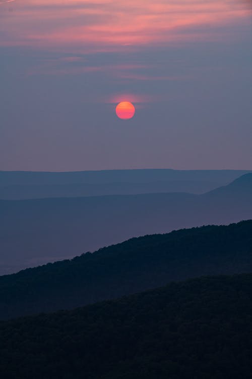 A sunset over a mountain range with a bright orange sun