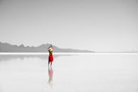 一名女子身着红裙，头戴帽子，静静站在沙漠中反光的湖水里