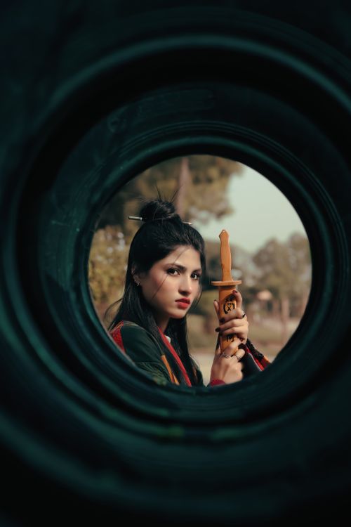 Free Woman holding a katana, captured through a circular frame, with a focused and intense expression, outdoors. Stock Photo