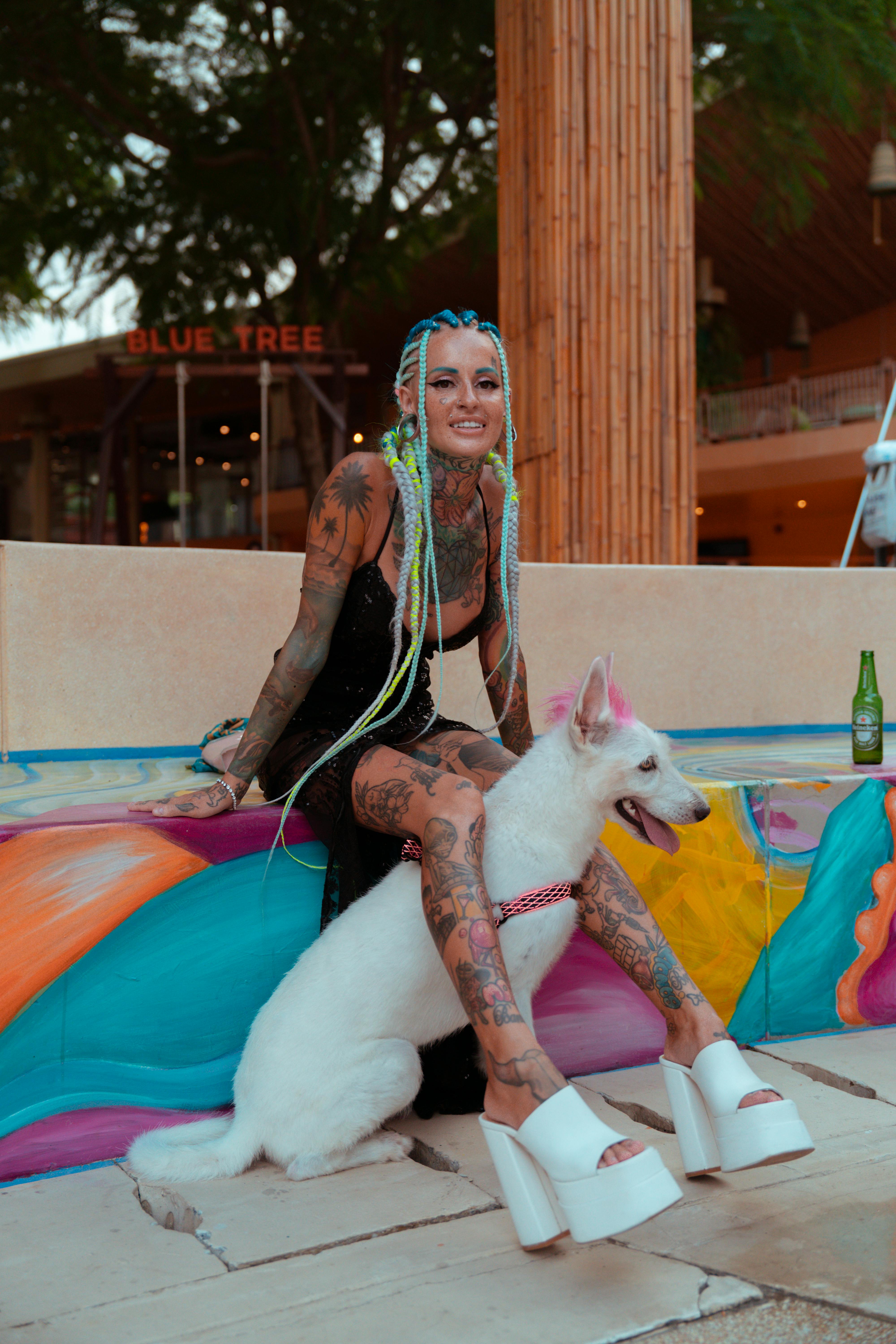 a tattooed woman with colorful hair sitting next to her dog