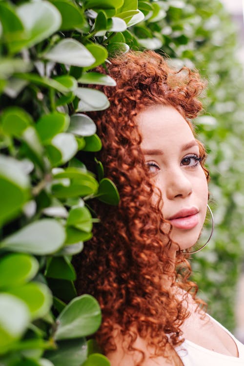 a curly haired woman posing near a tree