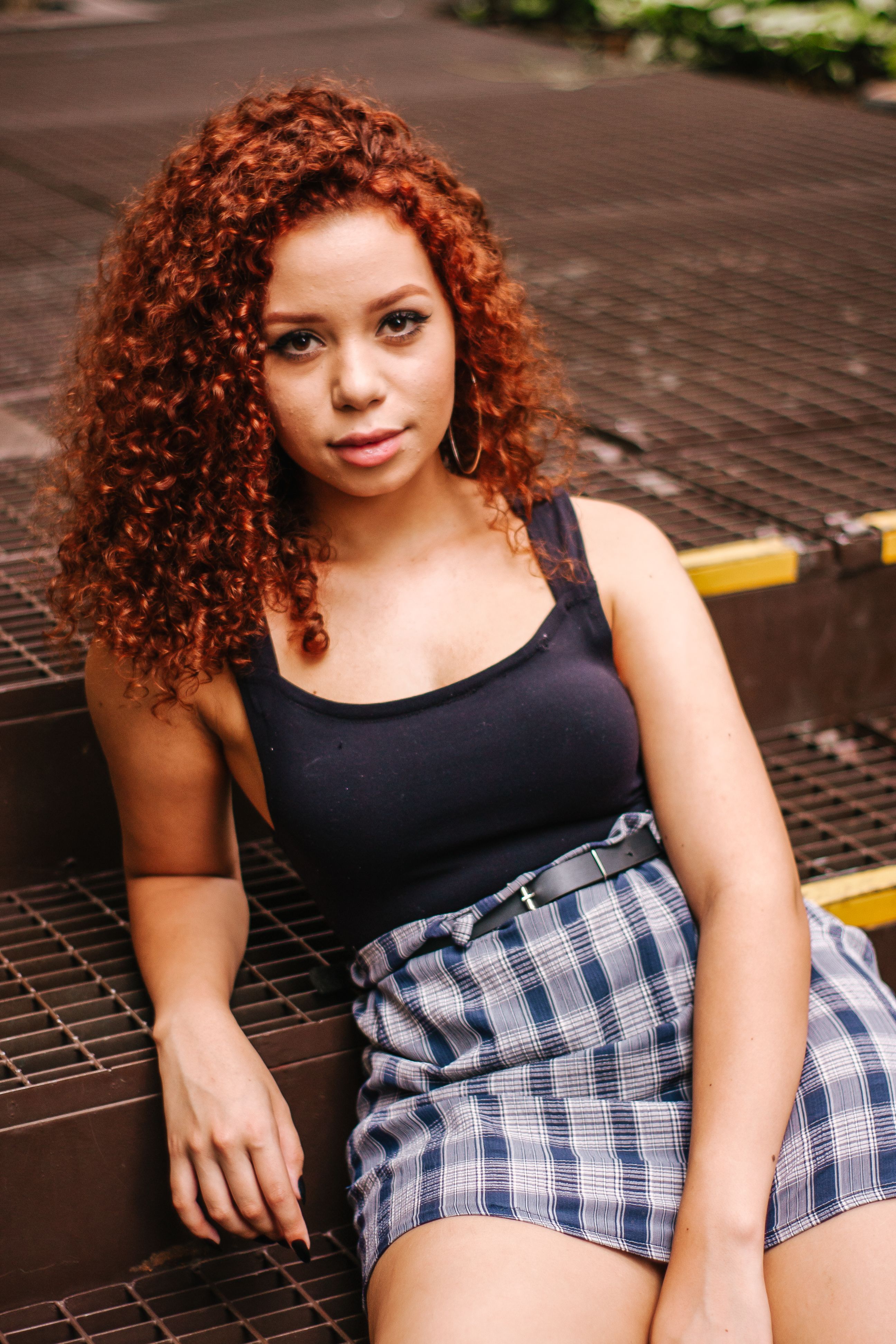 Portrait of a fashionable woman with curly hair posing casually outdoors on steps.