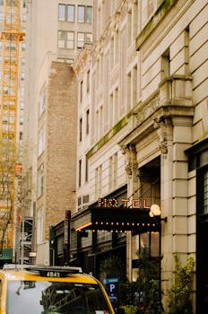Vertical view of an urban street with a historic hotel sign and yellow taxi.