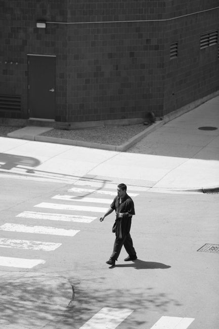 A man walks across a sunlit city crosswalk, captured in black and white.