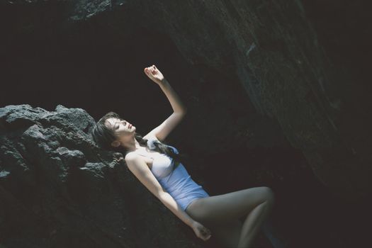 Young woman in white swimsuit leaning gracefully against rocks in serene outdoor setting.