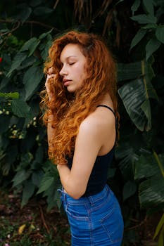 侧面轮廓是一位红发卷曲的美丽女子，站在生机盎然的树叶前