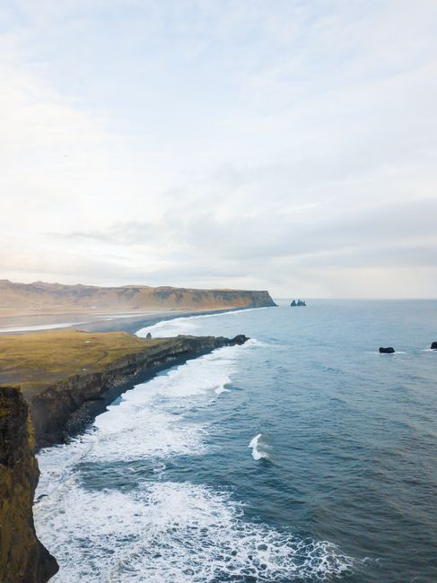 Breathtaking aerial view of Iceland's rugged coastal cliffs and expansive ocean under a cloudy sky.