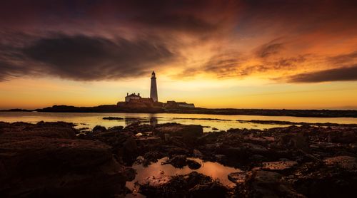 Free A dramatic seascape with a lighthouse silhouette during a vibrant sunset. Stock Photo