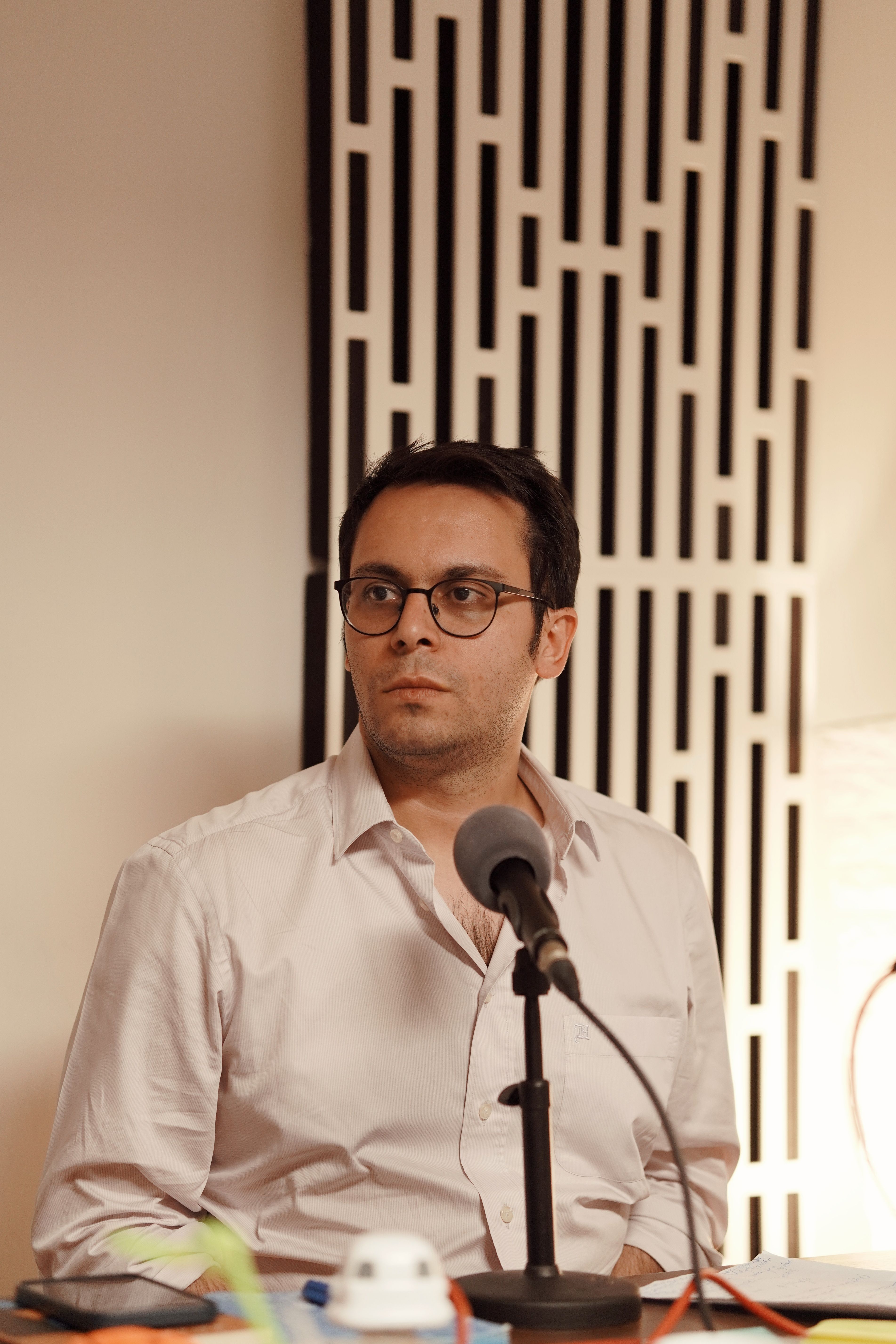 Adult man with eyeglasses in a podcast recording session indoors.
