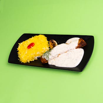 Elegant food photography of chicken and rice dish on black plate with green backdrop.