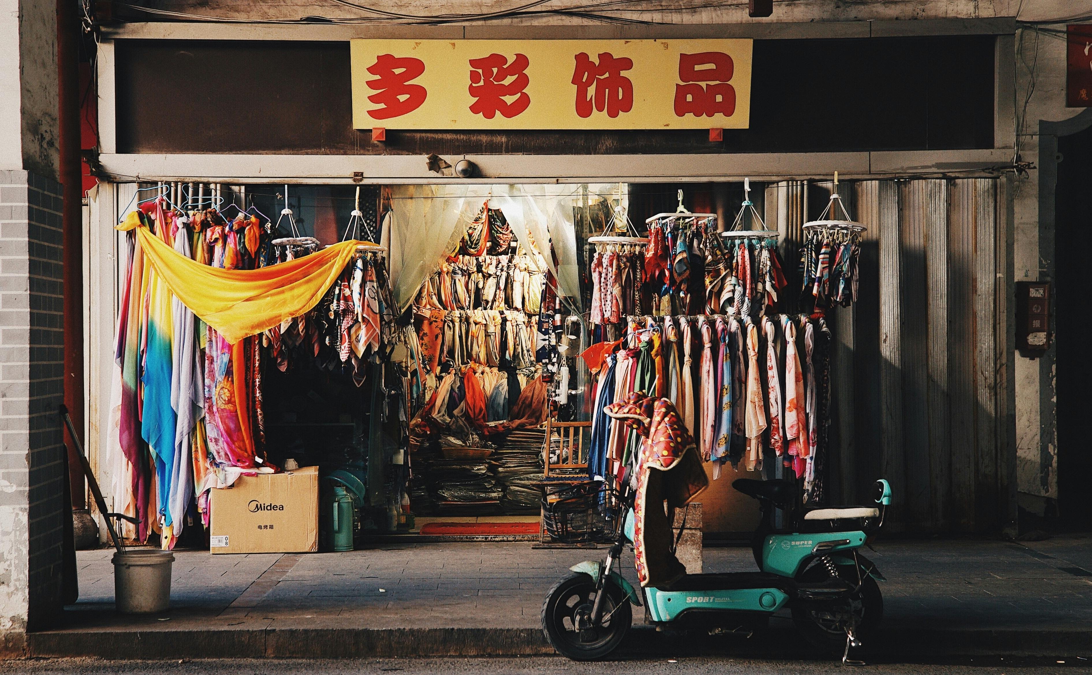 Vibrant clothing store facade with hanging fabric and parked scooter.