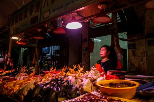 Free Asian woman selling poultry at a vibrant night bazaar food stall, illuminated by warm lights. Stock Photo
