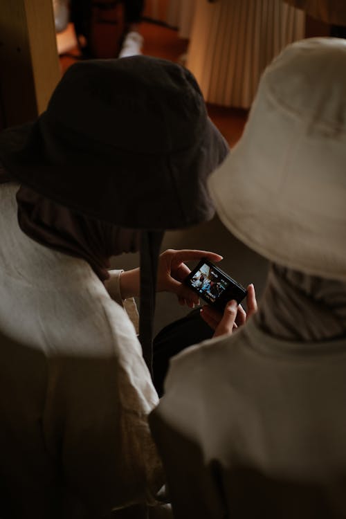 Two people wearing hats are looking at a cell phone