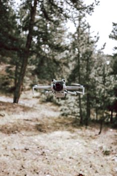 An advanced drone hovering among trees in a dense forest, showcasing technology in nature.