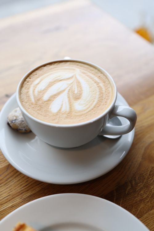 Free A beautifully crafted cappuccino with intricate latte art served in a white cup on a wooden table. Stock Photo