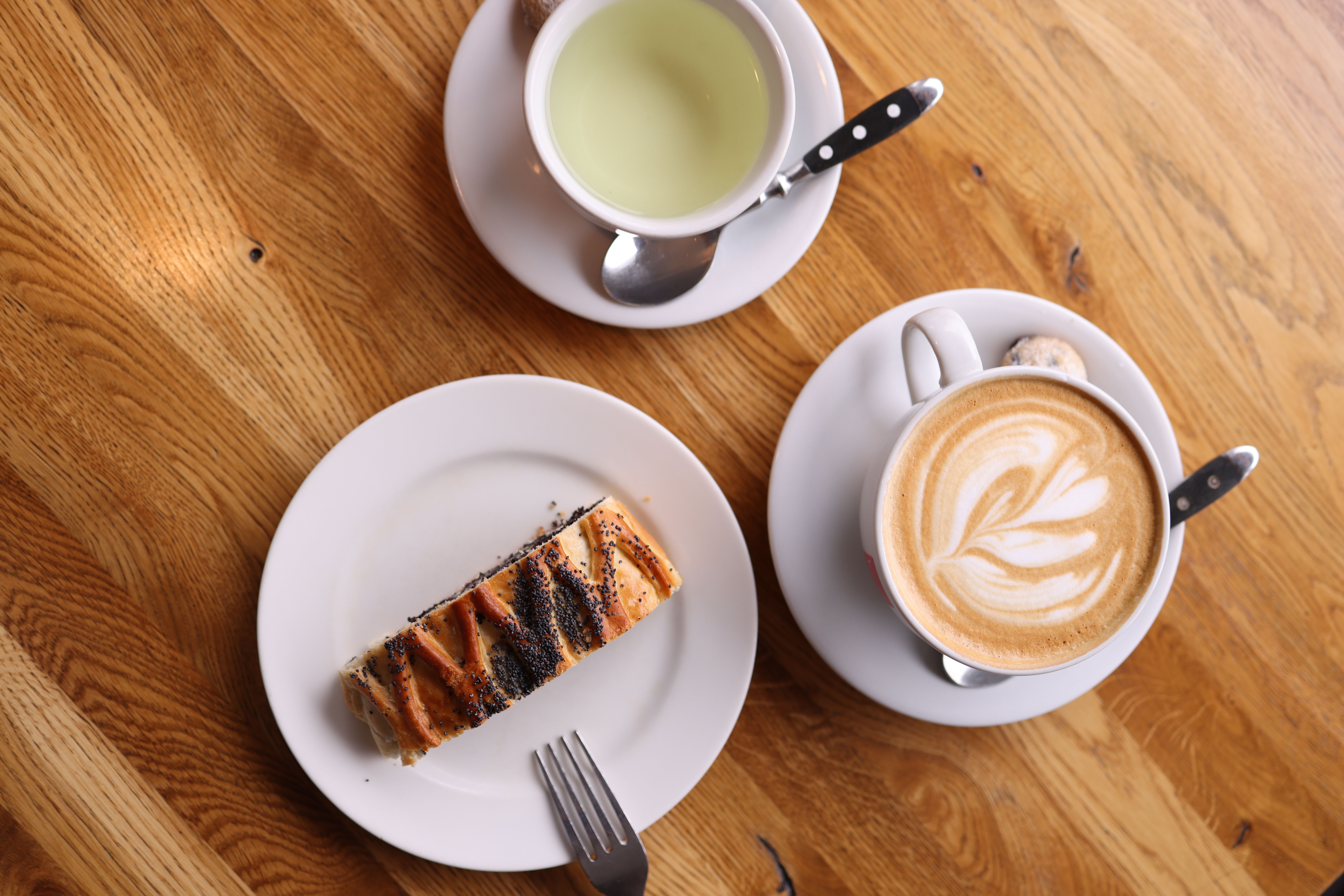 Overhead tea-and-coffee pairing: a cappuccino with latte art, a cup of green tea, and a slice of pastry