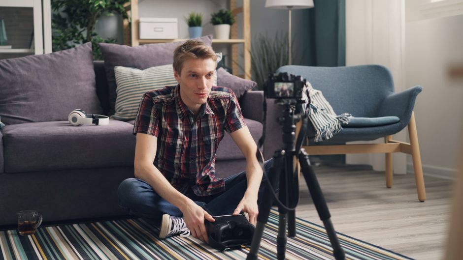 How to Write YouTube Descriptions That Rank on Google Search Young man sitting on the floor filming a vlog in a cozy living room with camera and tripod.