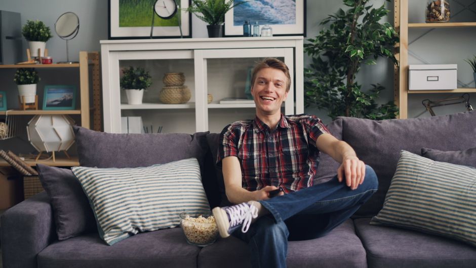 A cheerful man sits on a sofa with popcorn, enjoying his leisure time in a stylish living room.