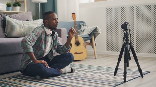 A young man wearing headphones records a video in a cozy home setting with guitar props.