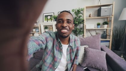 A cheerful man takes a selfie at home, sitting on a comfortable sofa surrounded by plants and decor — photo by Vitaly Gariev on Pexels
