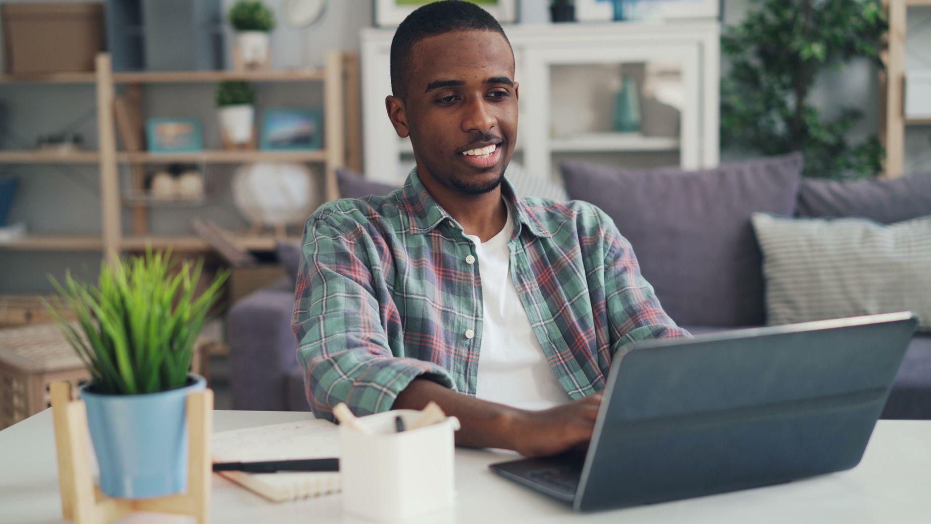 Young man smiling while using laptop in a modern home office setting.