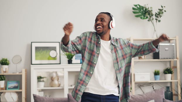 A joyful man wearing headphones dances indoors, expressing happiness and enjoyment.