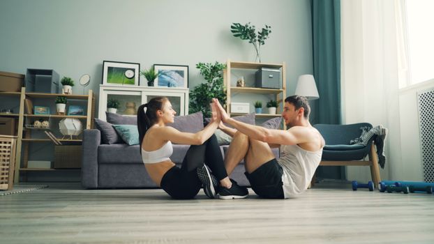 A couple working out together at home, performing exercises on the floor with high-fives.