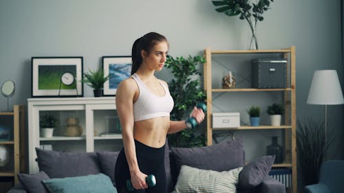 A woman is standing in front of a couch with dumbbells