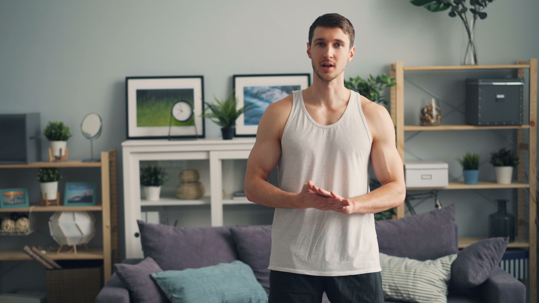 Muscular man in a tank top standing in a modern living room, ready for exercise.