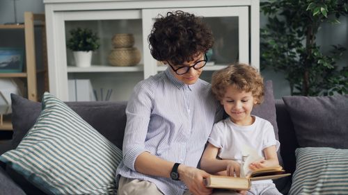 Free A mother and child enjoying a book together on a comfortable sofa at home. Stock Photo