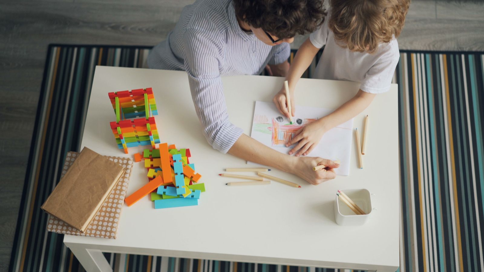 A mother and child drawing together with colored pencils during a creative learning activity at home