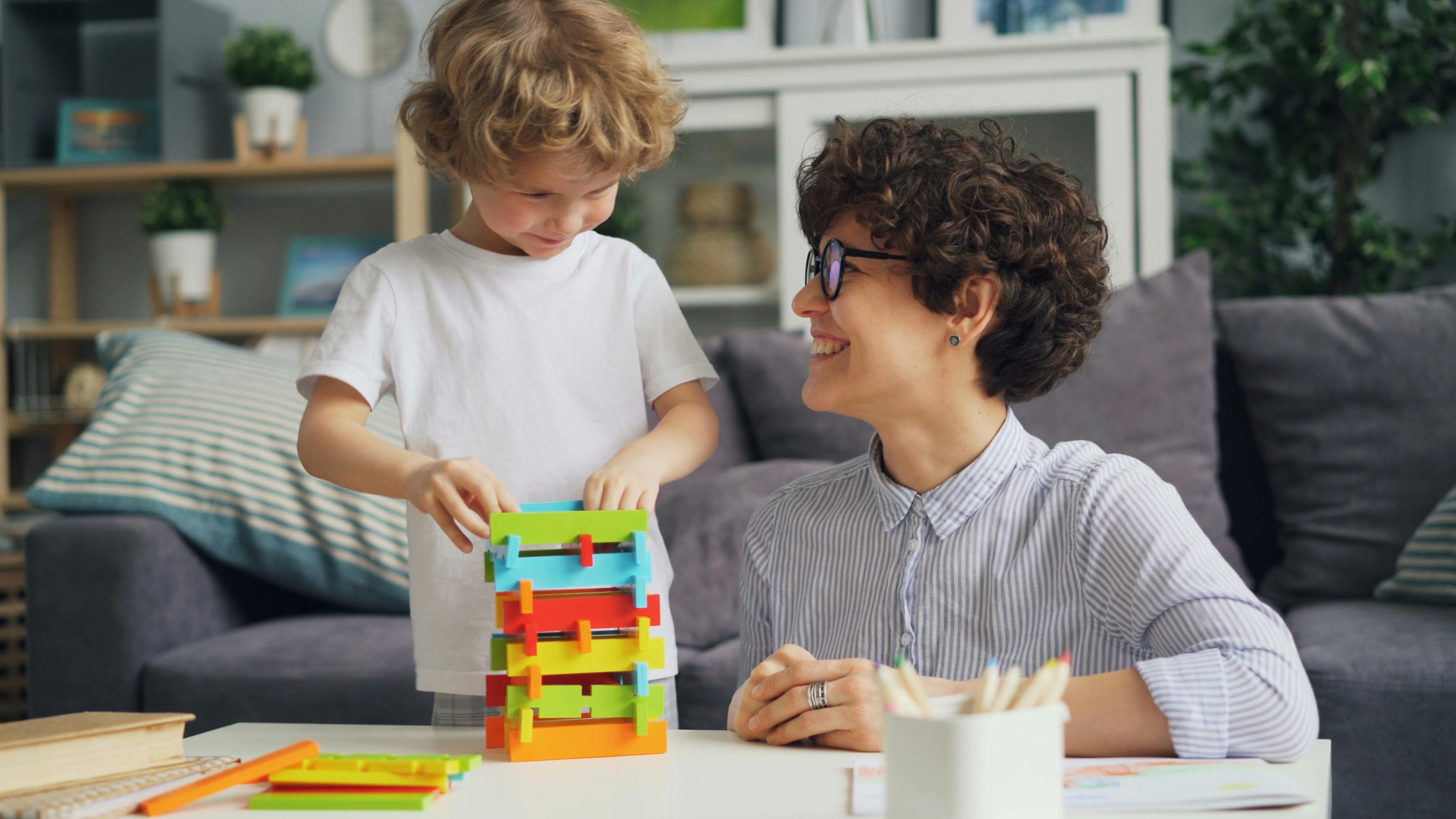 smiling mother sitting with son and playing with blocks