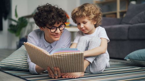 Free A mother and her young son enjoy reading a book together on the carpet indoors. Stock Photo