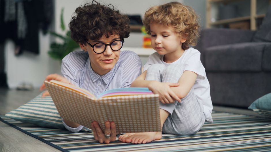 Mother and young son lying on carpet, engaged in reading a book together happily.
