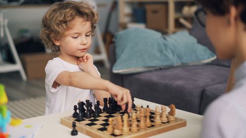 Free Young child playing chess indoors, deeply focused on making the next strategic move. Stock Photo