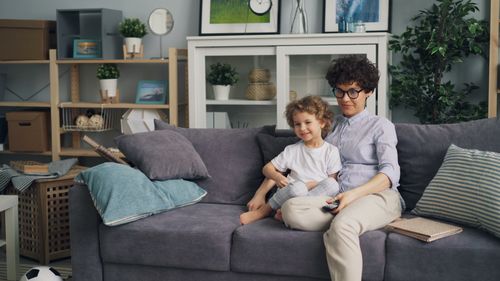 Free Mother and son sitting on a couch in a cozy living room, enjoying their time together. Stock Photo