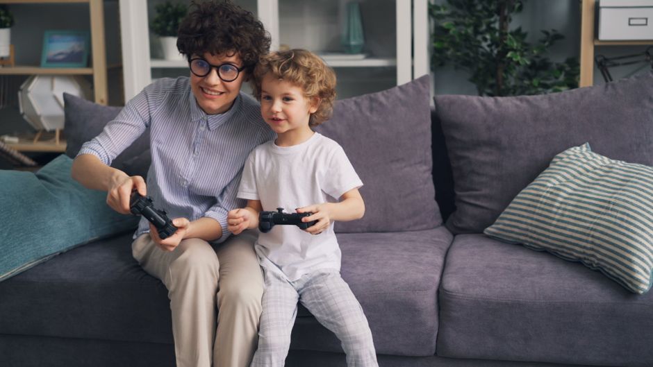 Happy mother and son bonding over video games on the couch, having fun indoors.