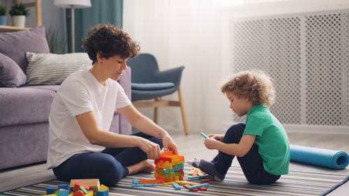 Free A woman and child engage in playful block building in a cozy living room setting. Stock Photo