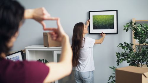 Free A couple enthusiastically hanging artwork while decorating their new home together. Stock Photo