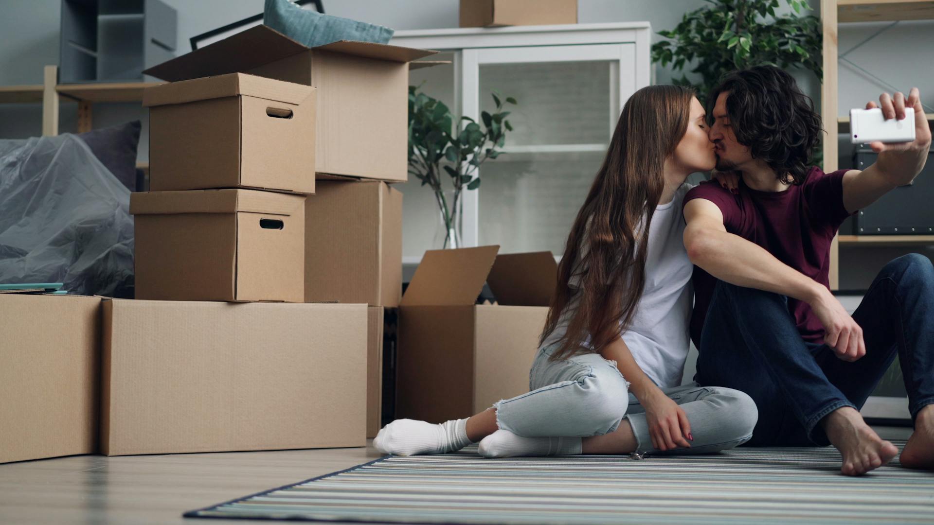 A young couple captures a selfie during their moving day, surrounded by boxes.