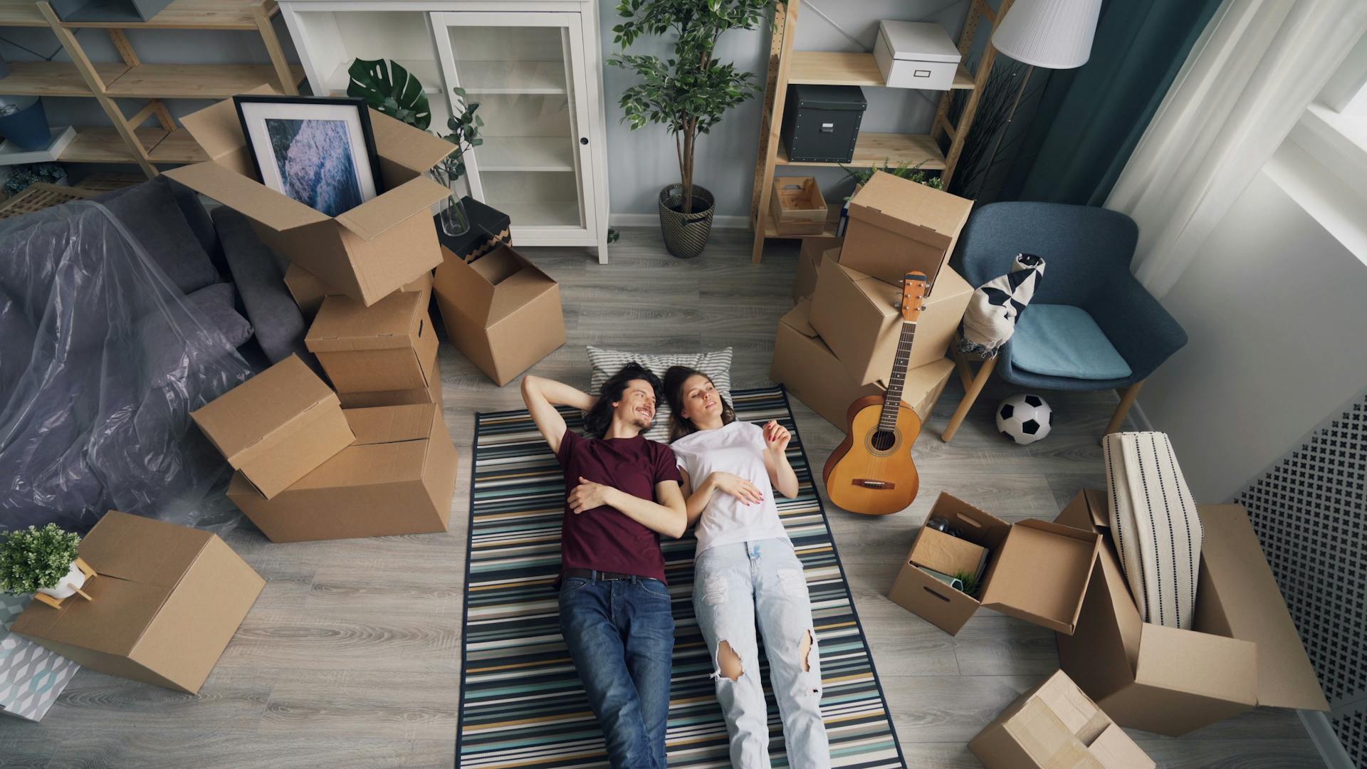 A young couple lying on a rug surrounded by moving boxes, embodying a fresh start in their new home.